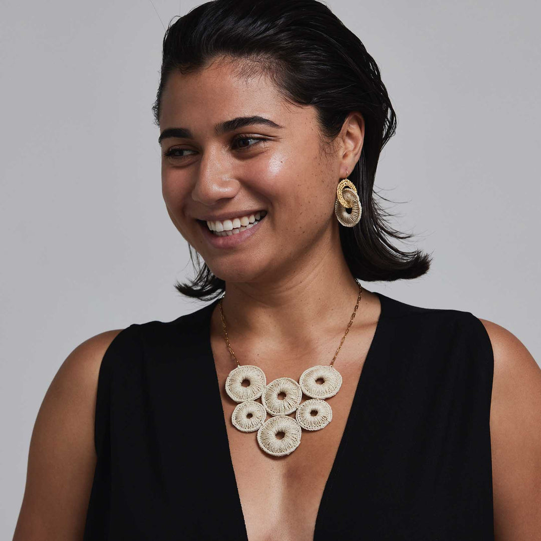 Woman wearing a black top and gold necklace with circular pendants against a gray background