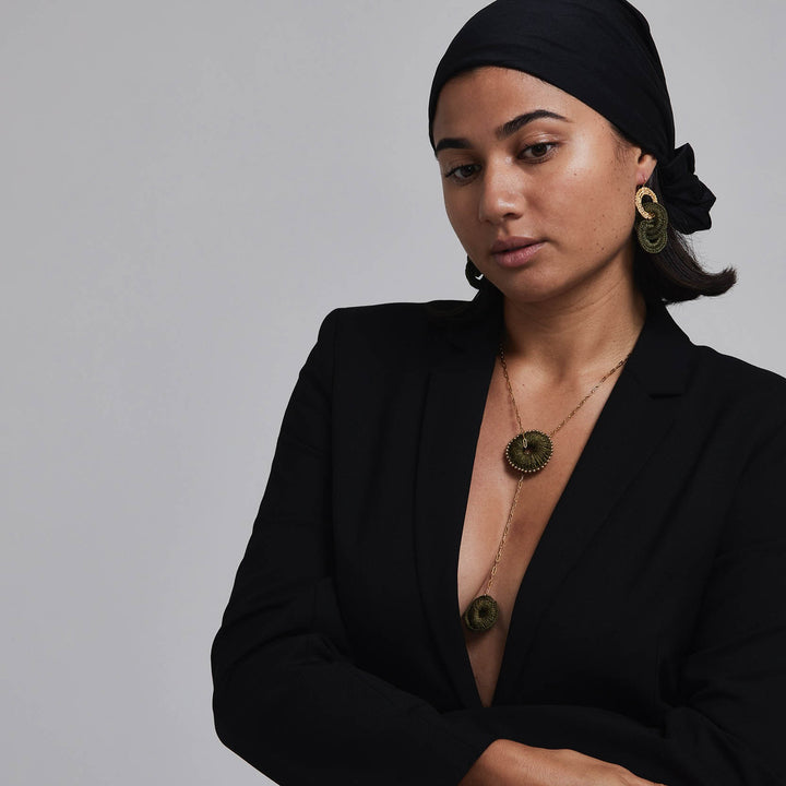 Woman wearing a black outfit with gold jewelry against a gray background
