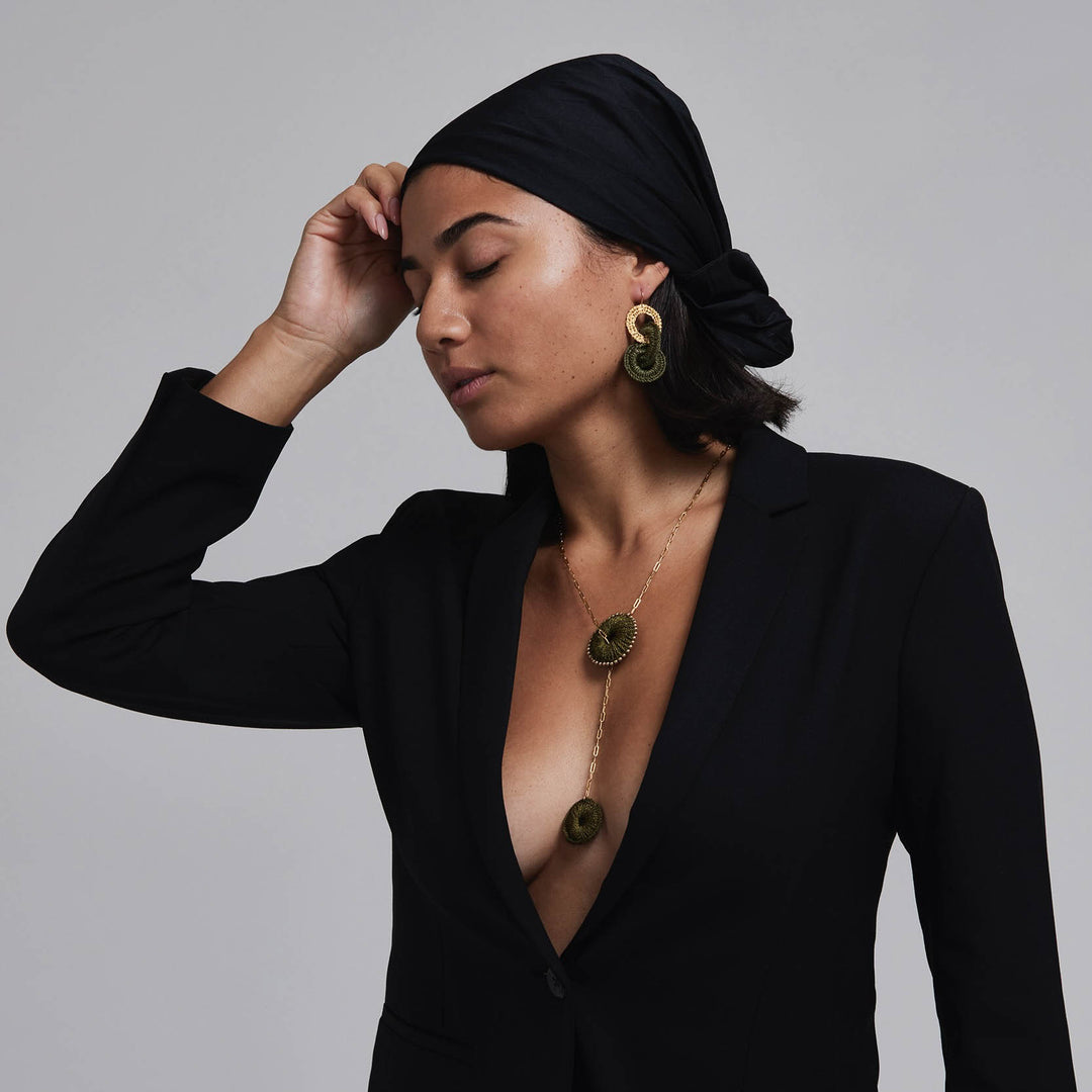 Woman wearing a black outfit with gold jewelry against a gray background