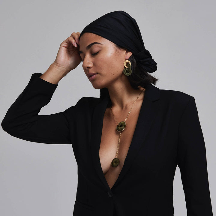Woman wearing a black outfit with gold jewelry against a gray background