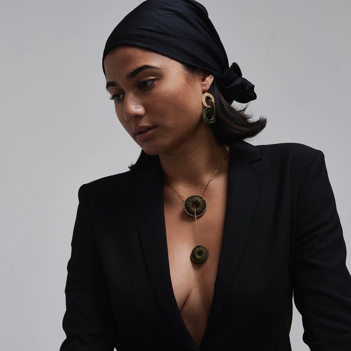 Woman wearing a black outfit with a deep neckline, gold necklace, and earrings on a gray background