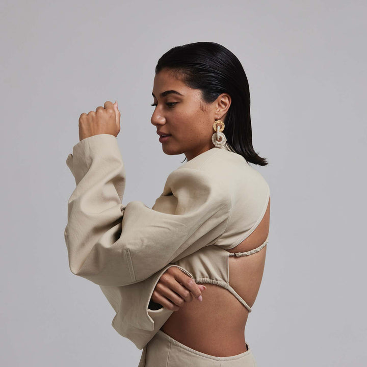 Woman wearing a beige outfit with cut-out design on a plain background