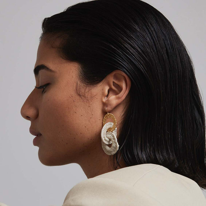 Woman wearing a large, intricate earring on a plain background