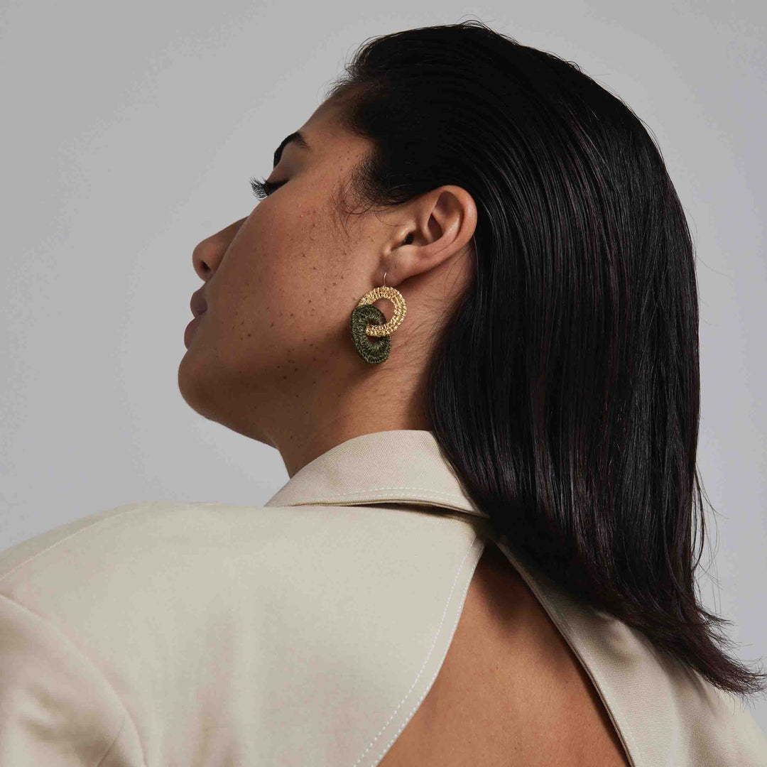 Woman wearing gold earrings with a green stone on a neutral background