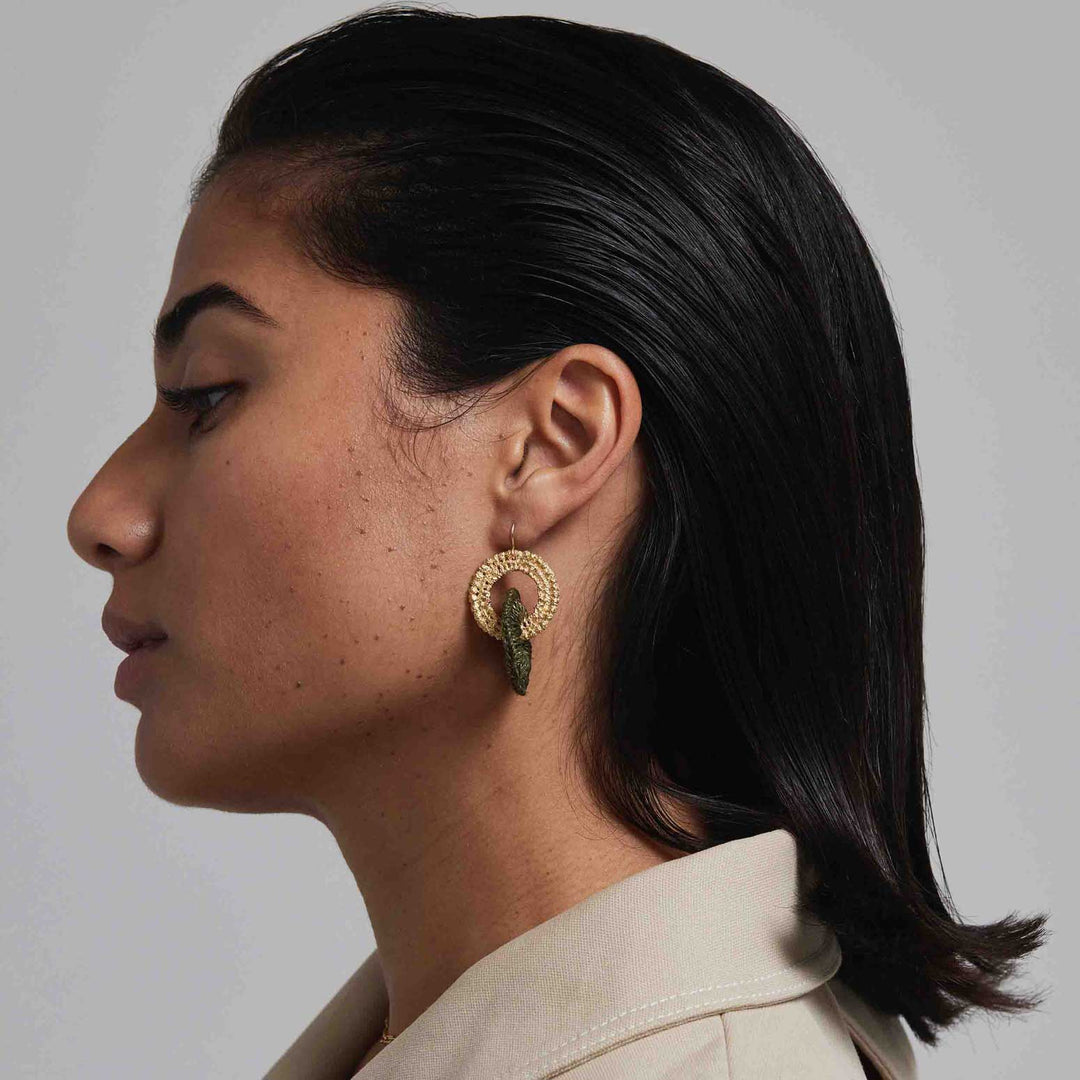 Side profile of a person wearing gold hoop earrings with a neutral background