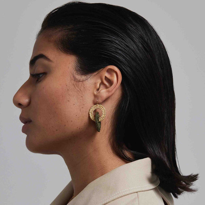 Side profile of a person wearing gold hoop earrings with a neutral background