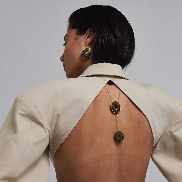 Woman wearing a beige open-back top with a necklace and earrings on a plain background