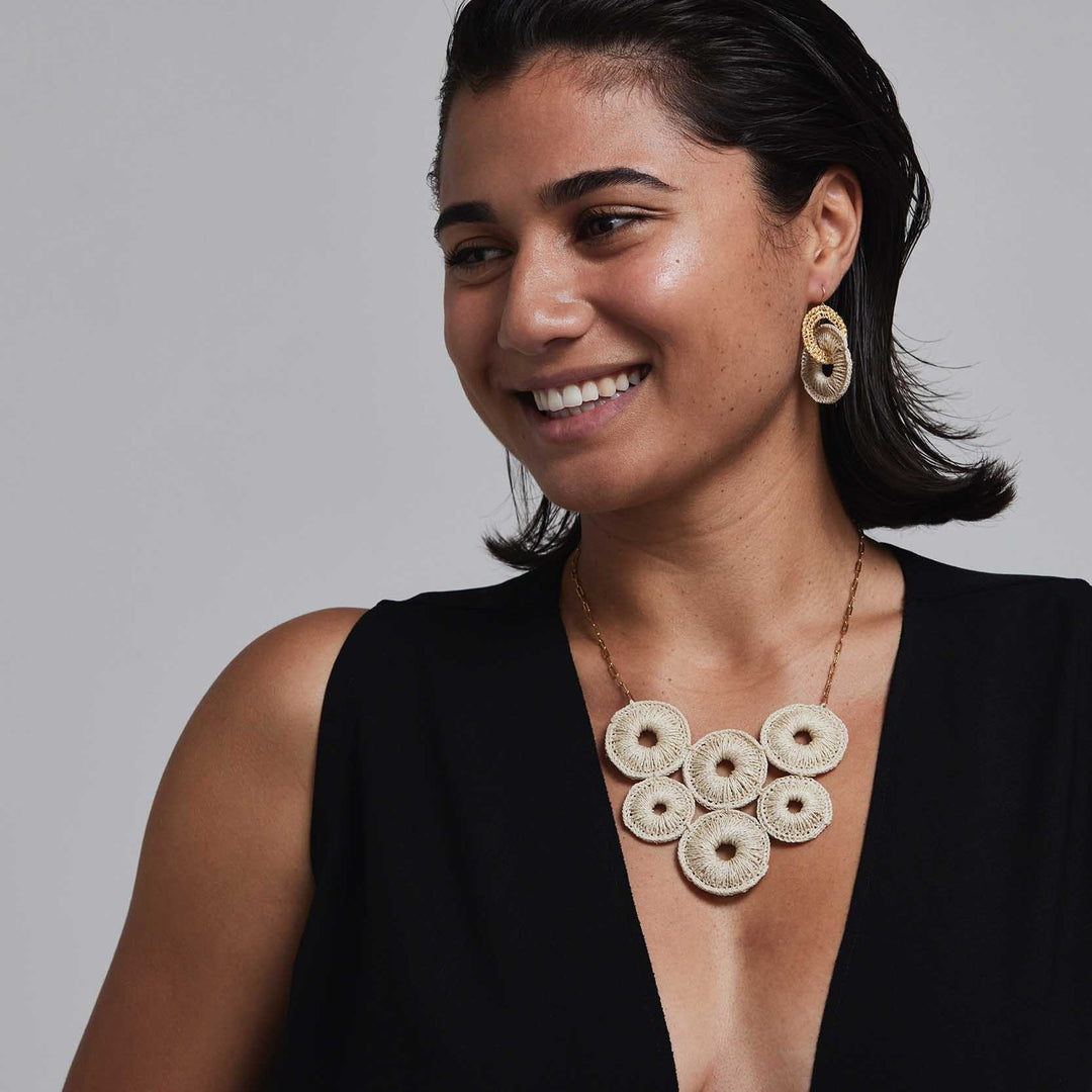 Woman wearing a black top and gold necklace with circular pendants against a gray background