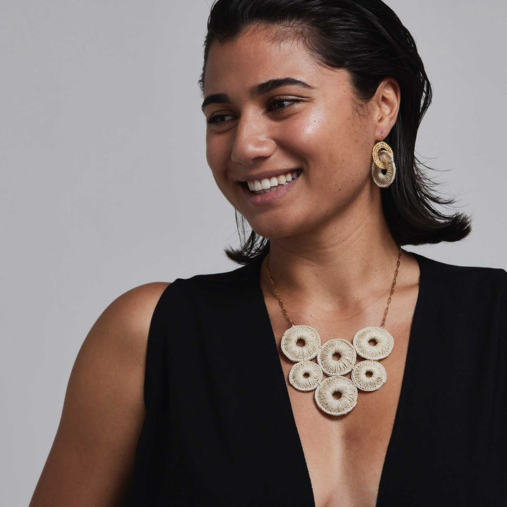 Woman wearing a black top and gold necklace with circular pendants against a gray background