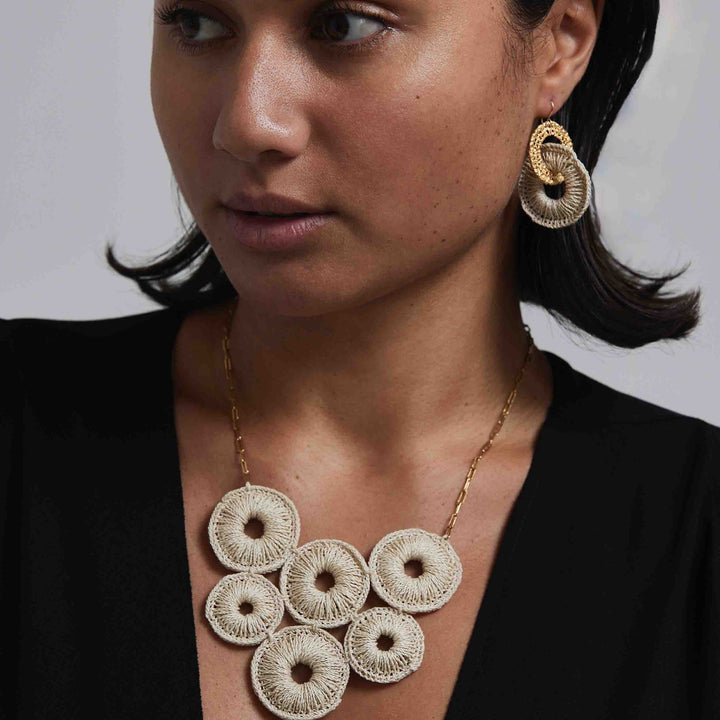 Woman wearing a gold necklace and earrings with a plain background