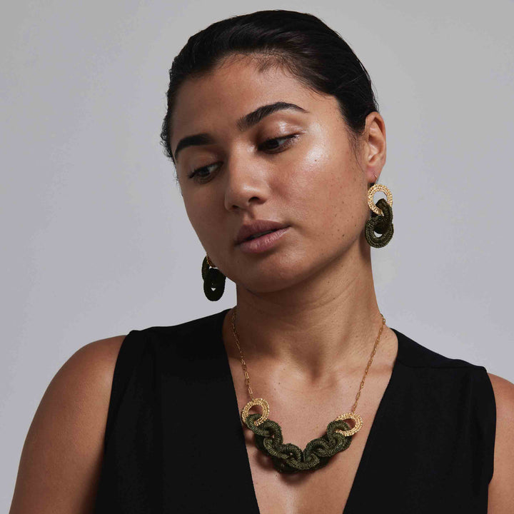 Woman wearing gold and green jewelry against a plain background