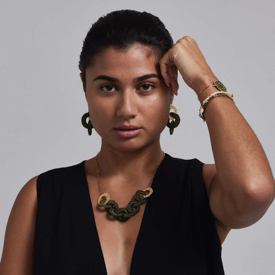 Woman wearing a black sleeveless top with green jewelry against a gray background
