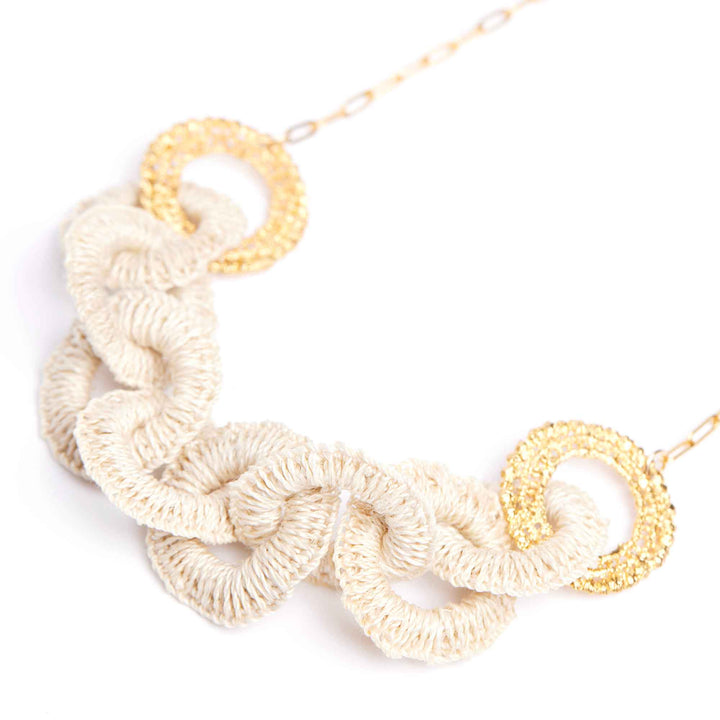 Necklace with white crocheted links and gold circular pendants on a white background