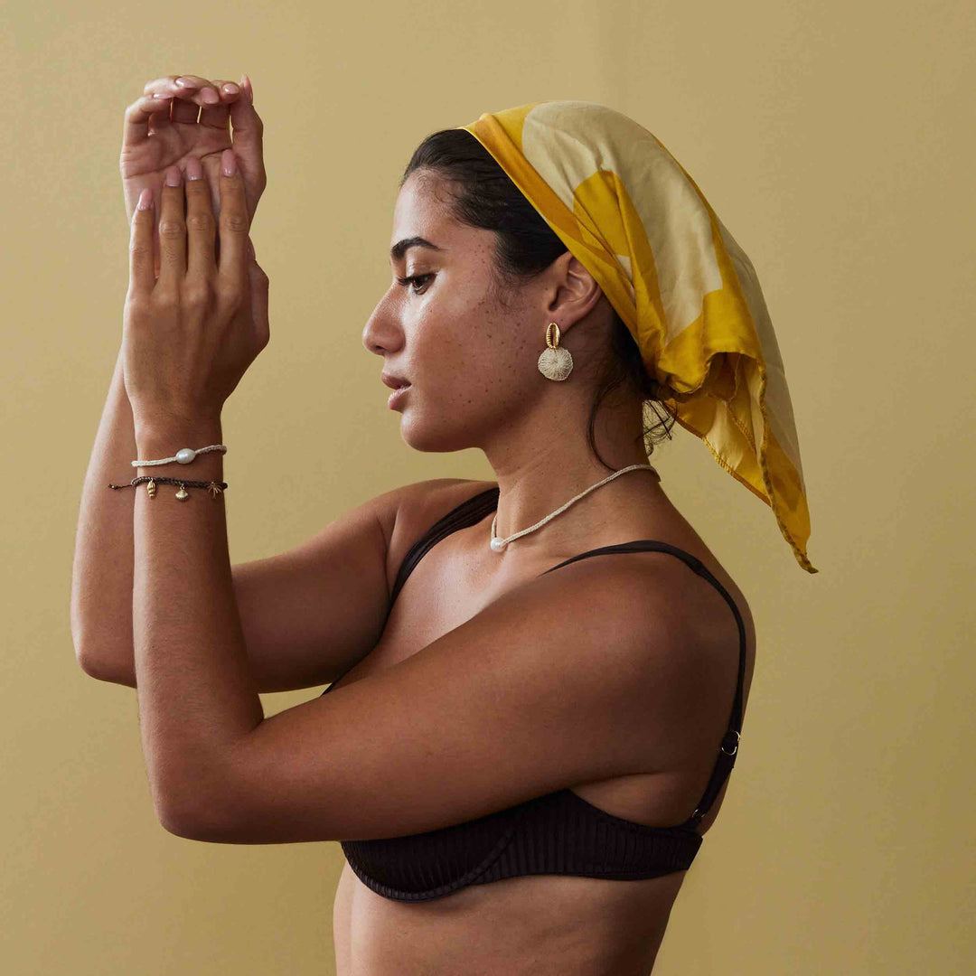 Woman with a yellow headscarf and black top against a beige background