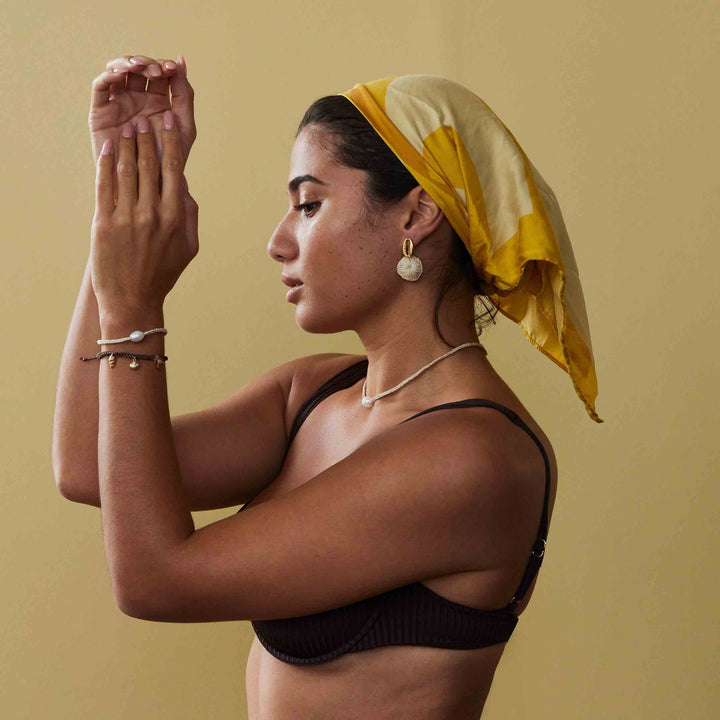 Woman with a yellow headscarf and black top against a beige background