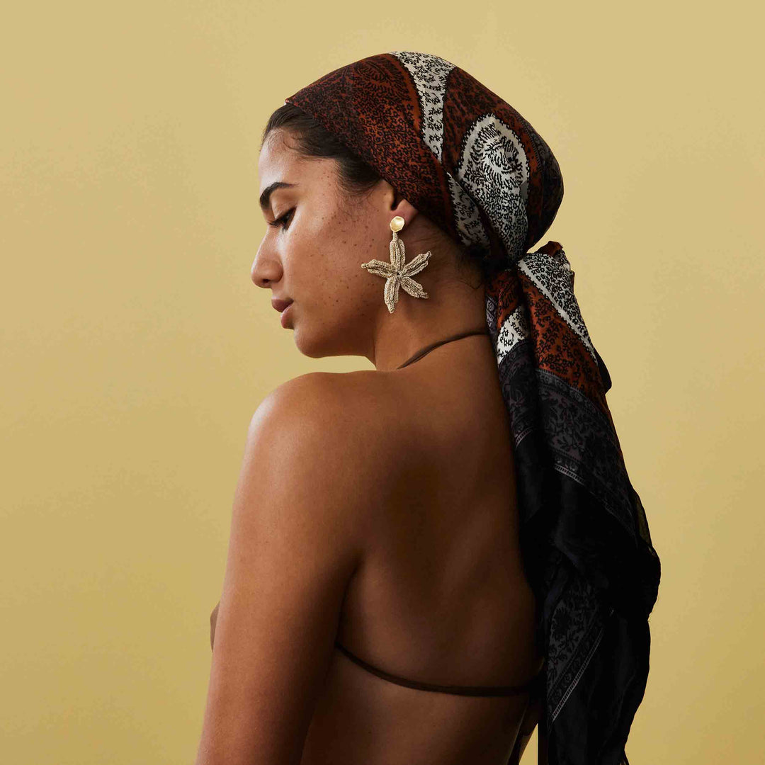 Woman wearing a patterned headscarf and starfish earrings against a beige background