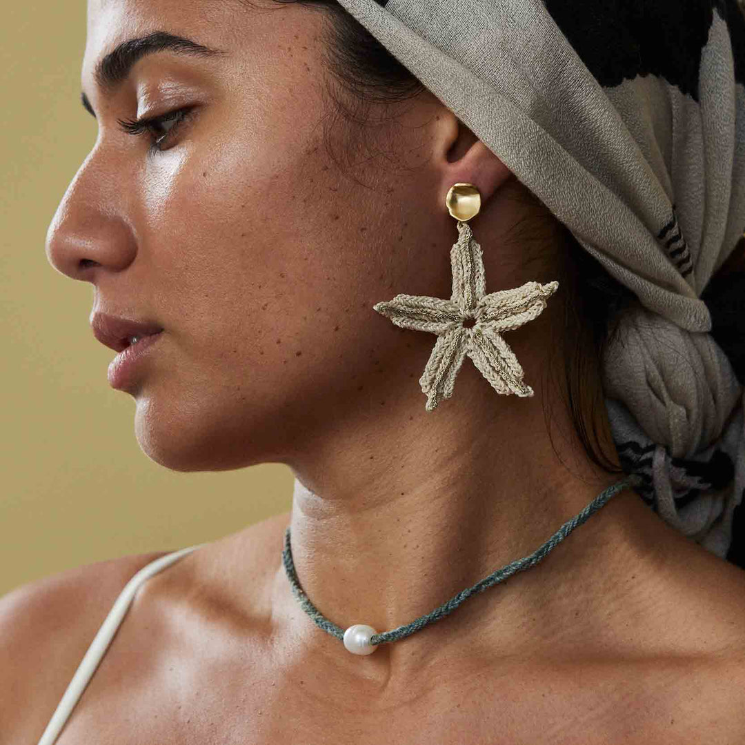 Woman wearing a gold starfish earring with a neutral background