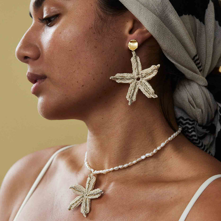 Woman wearing starfish-shaped earrings and a necklace with a beige background