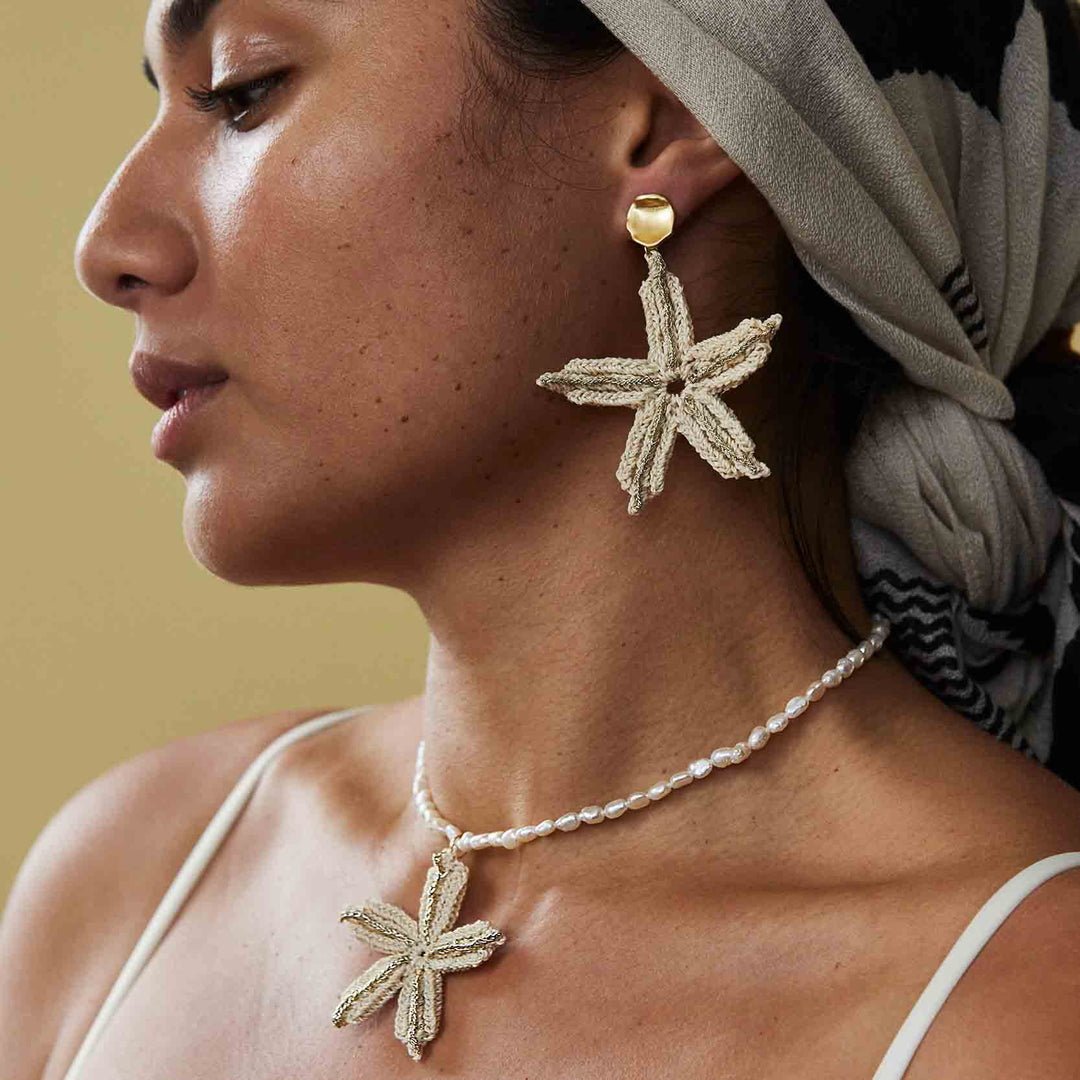 Woman wearing starfish-shaped earrings and a necklace with a beige background