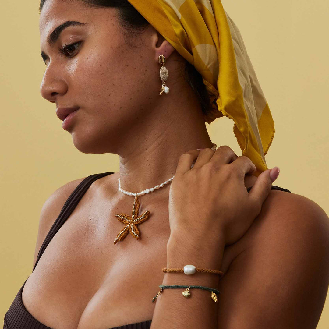 Woman wearing starfish necklace, earrings, and bracelets on a beige background