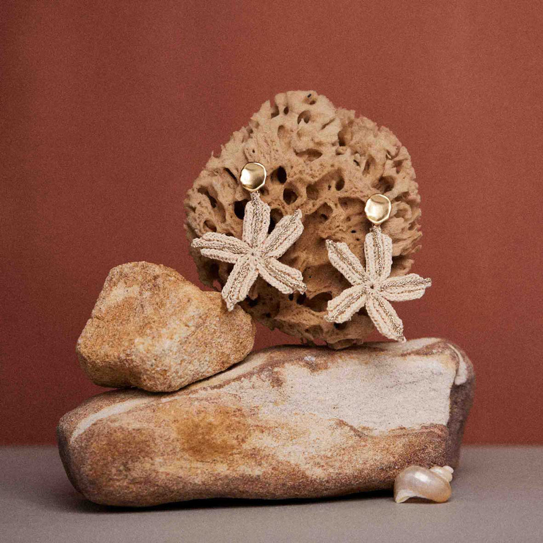 Pair of floral earrings on a textured stone surface with a brown background
