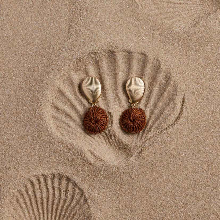 Pair of earrings with brown spherical charms and gold accents on a sandy background.