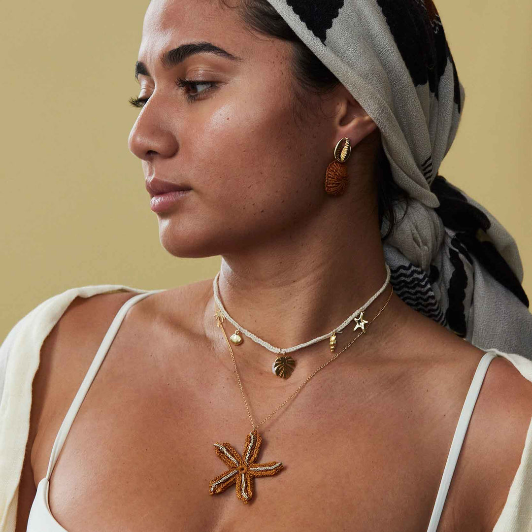 Woman wearing gold necklaces and earrings with a neutral background