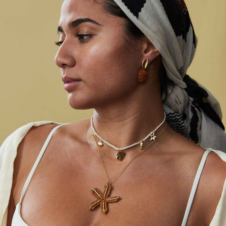 Woman wearing gold necklaces and earrings with a neutral background