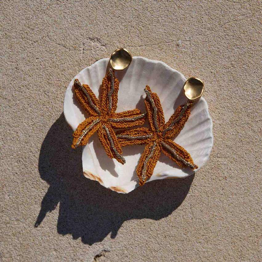 Starfish-shaped earrings on a white shell against a beige background