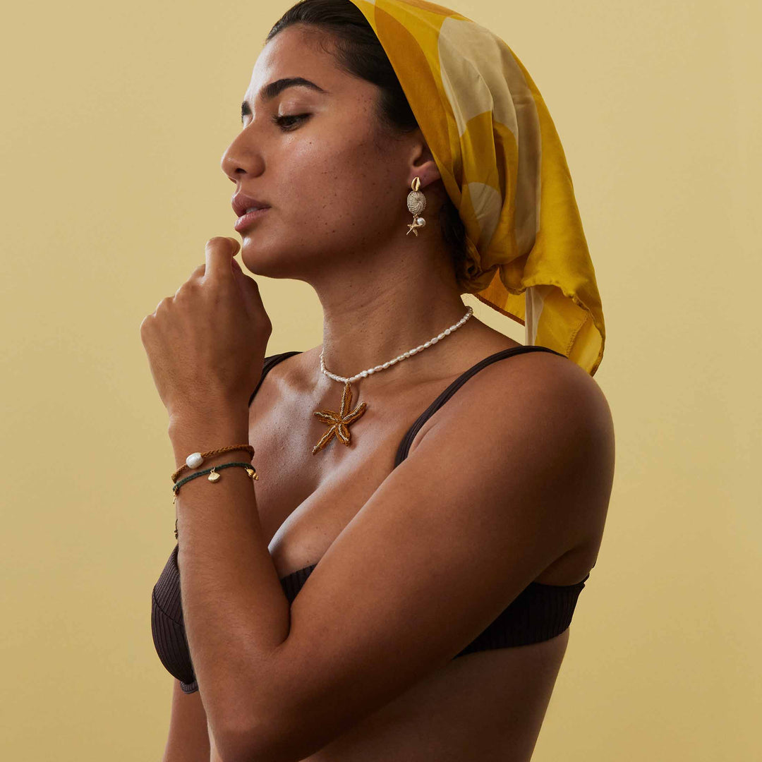 Woman wearing a yellow headscarf and black bikini against a beige background