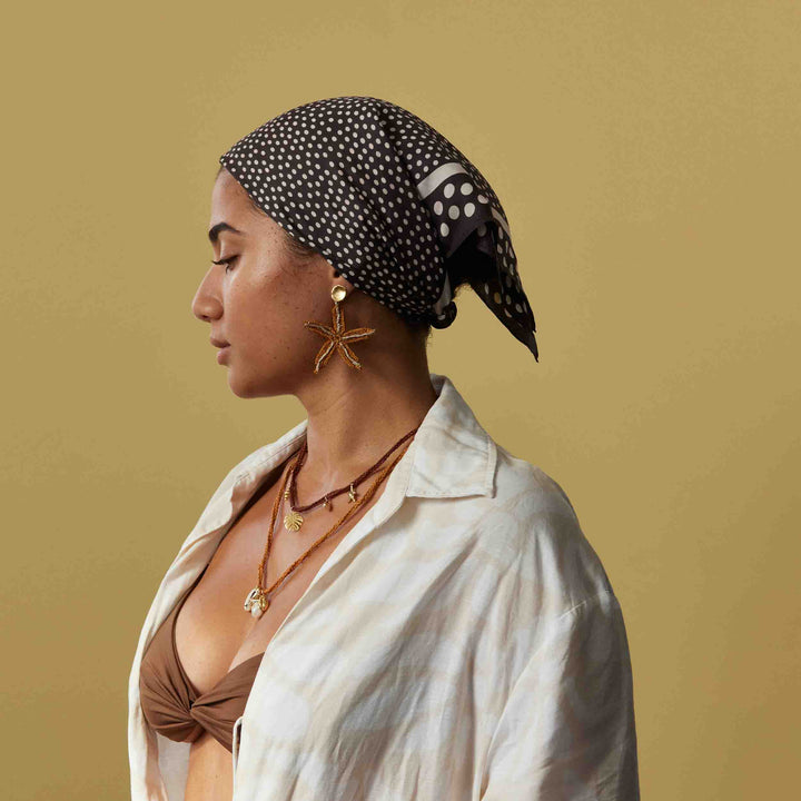 Woman wearing a polka dot headscarf and gold jewelry against a beige background