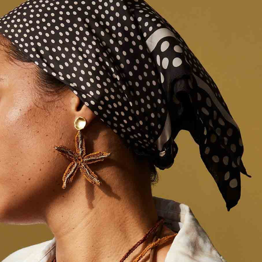 Woman wearing a patterned headscarf and layered necklaces against a beige background