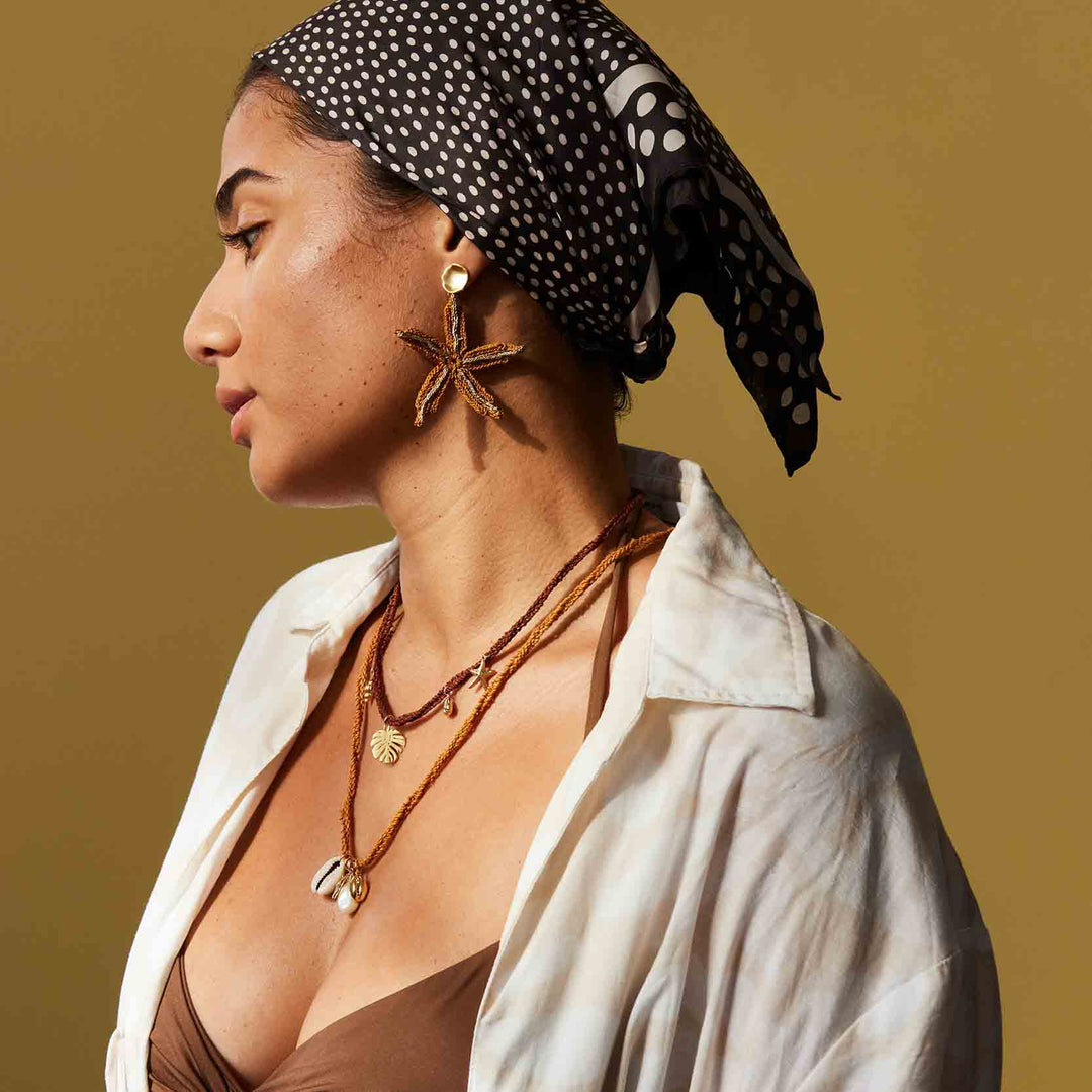 Woman wearing a patterned headscarf and layered necklaces against a beige background