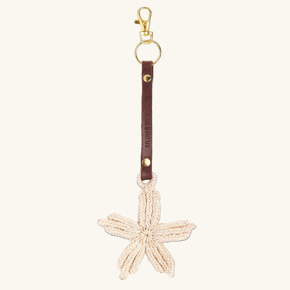 Starfish-shaped keychain with brown leather strap and gold clasp on a white background