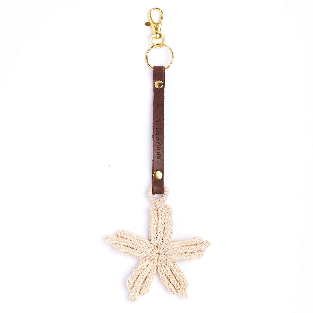 Starfish-shaped keychain with brown leather strap and gold clasp on a white background