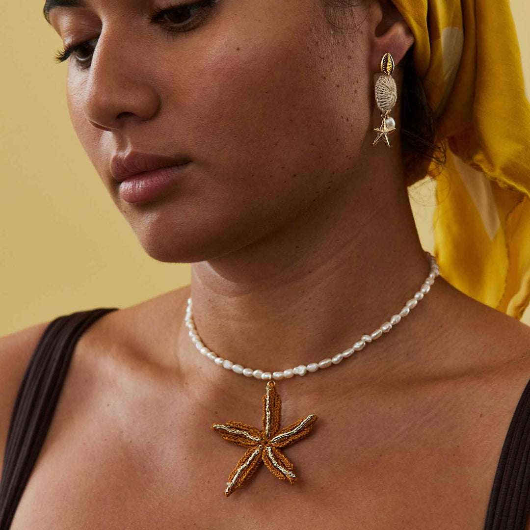 Woman wearing a starfish pendant necklace and matching earrings against a yellow background