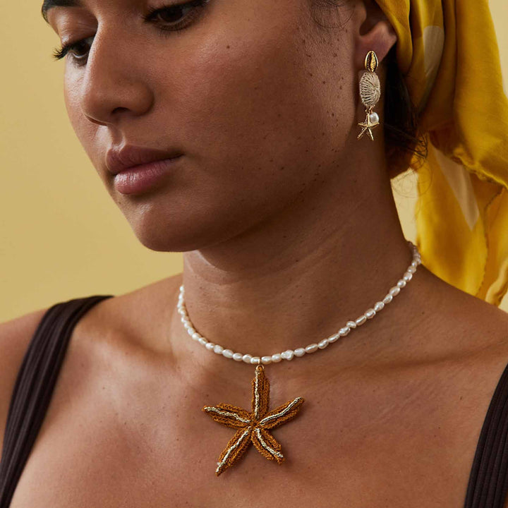 Woman wearing a starfish pendant necklace and matching earrings against a yellow background