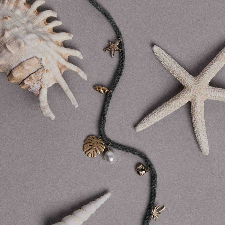 Necklace with shell and starfish charms on a gray surface with shells and a starfish.