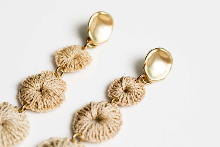 Detailed close up of Bilum and Bilas Sowana earrings. Warped gold earring with a trio of handwoven natural fibre dangling discs