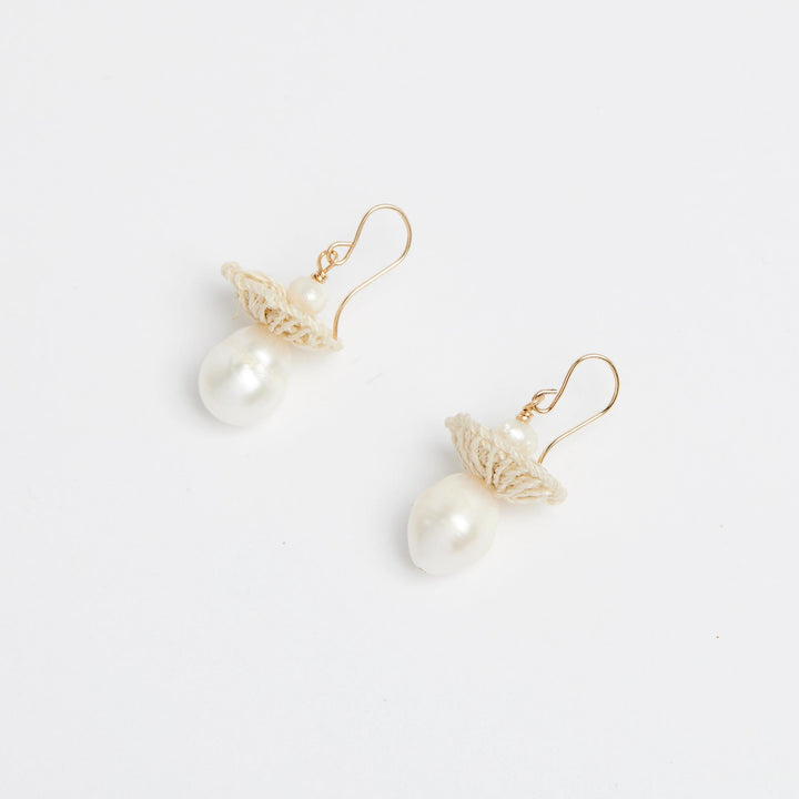 Side view of gold pearl drop earrings with woven natural fibre disc