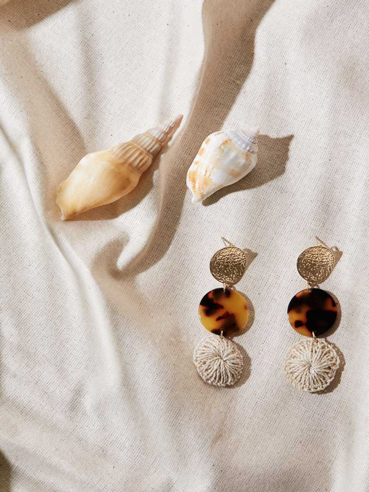 Bilum and Bilas three disc drop earrings with gold, fake turtle shell and textile bead displayed on linen with shells