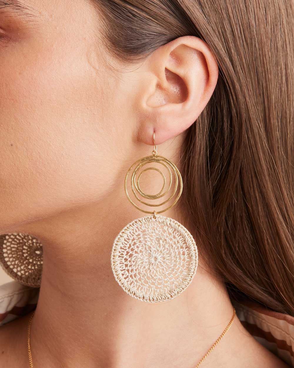 Model wearing gold swirl earrings with natural fibre woven disc on a profile view