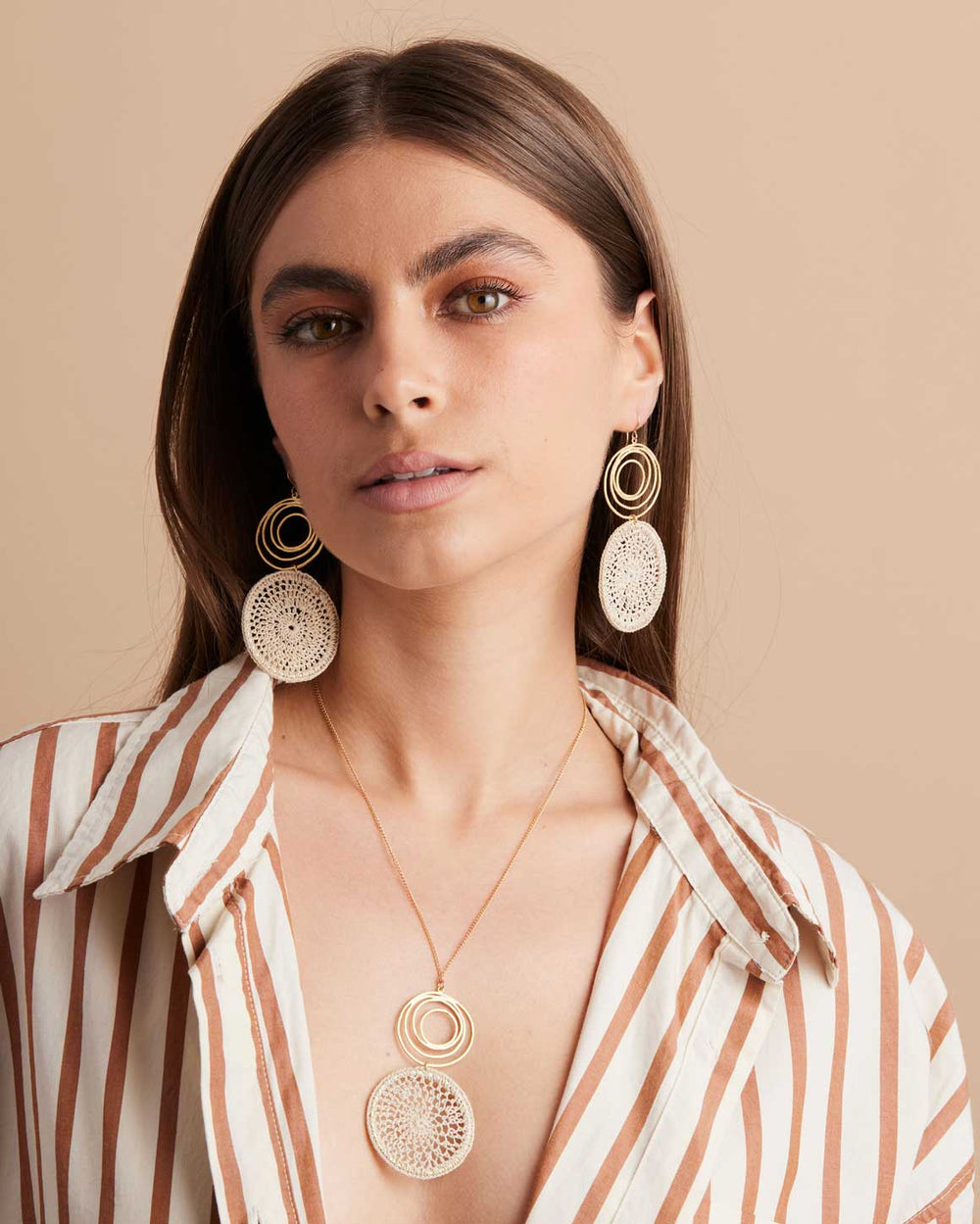 Model wearing gold filled fine chain necklace with gold swirl and natural fibre woven disc pendant and matching earrings