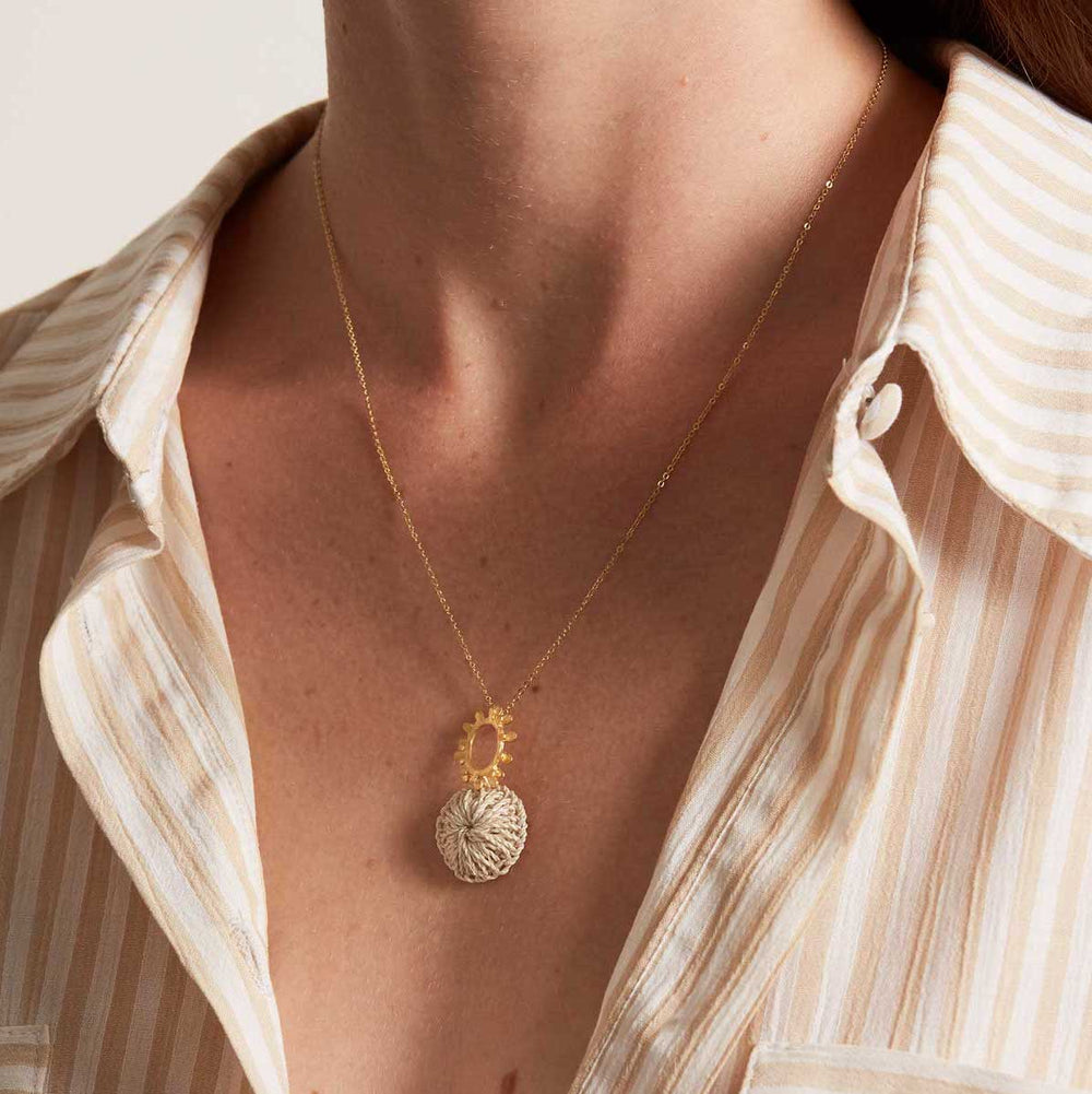 Model wearing gold textured sun pendant with natural fibre woven disc on a gold filled chain necklace
