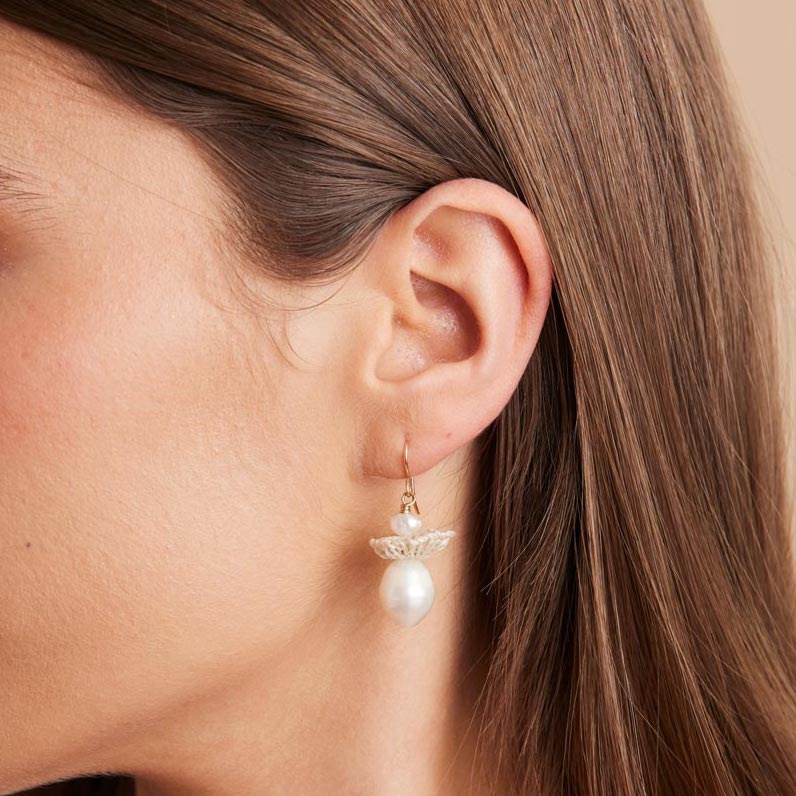 Model profile of gold pearl drop earrings with woven natural fibre disc