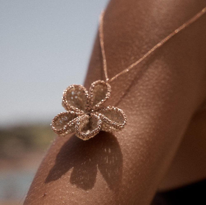 Rose gold woven flower necklace placed on an arm bilum and bilas