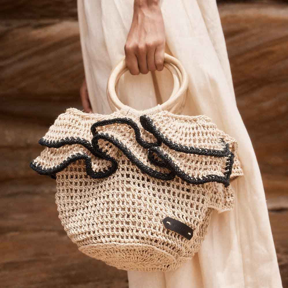 Woven basket with black ruffle trims being held on display by model in front of rocks.