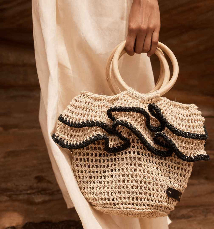 Woven basket with black ruffle trims being held by model in a white dress.