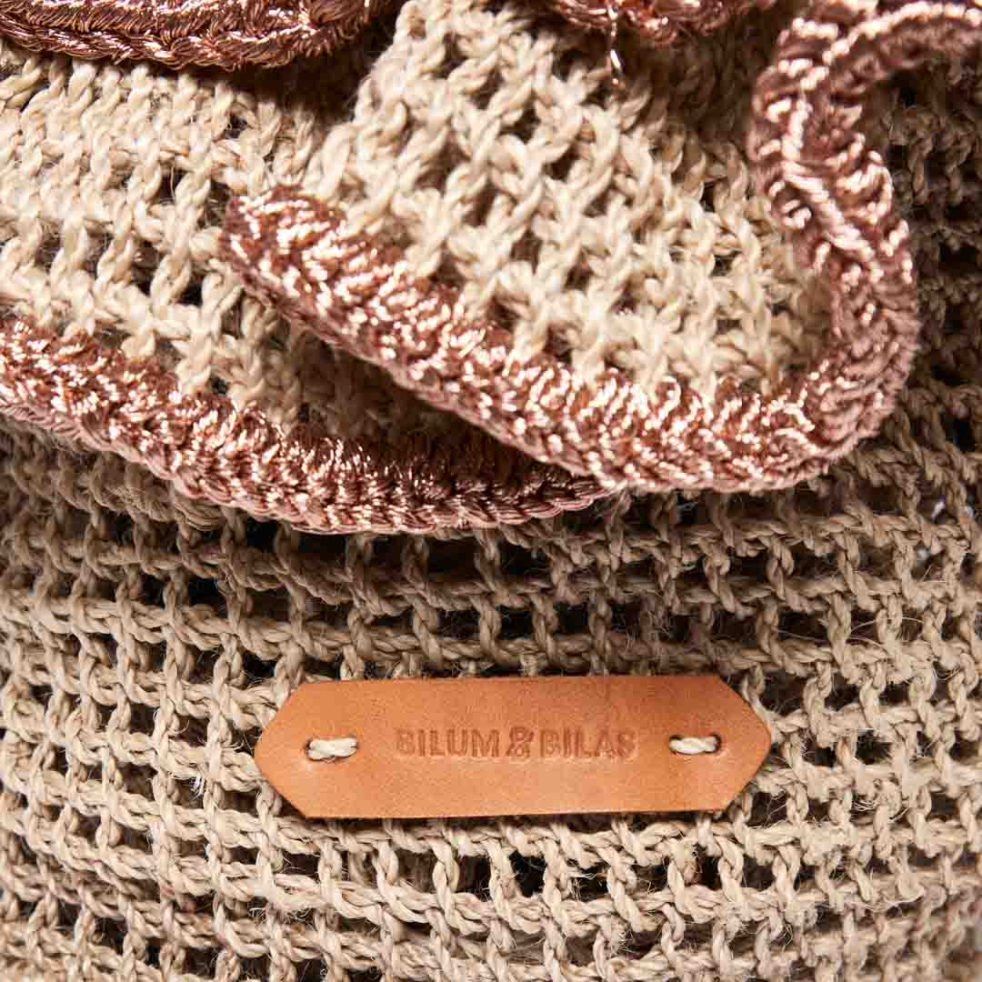 Handwoven basket with rose gold metallic trims and leather logo tag close up.