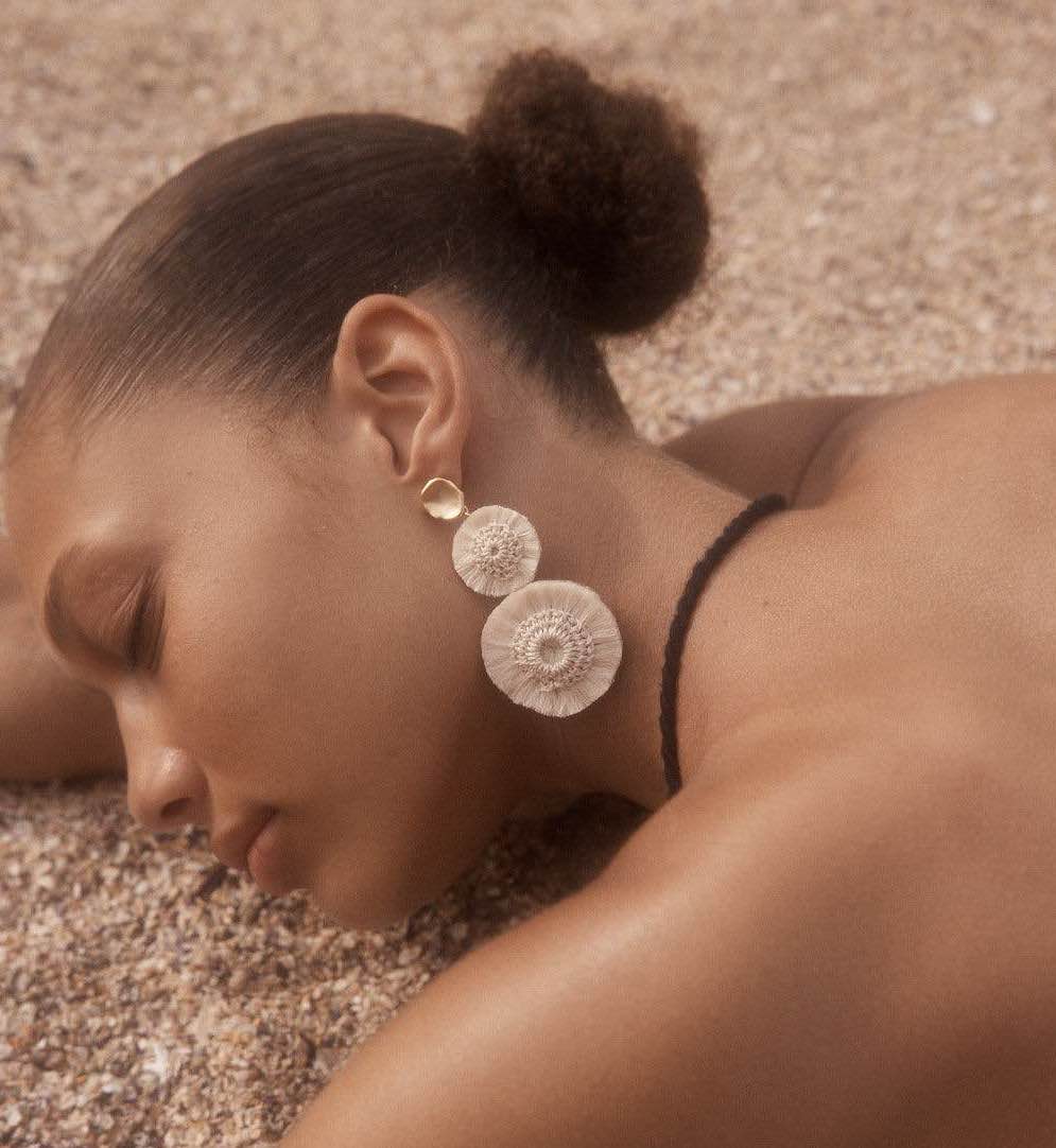 Model lying on sand wearing natural fibre pom pom earrings bilum and bilas